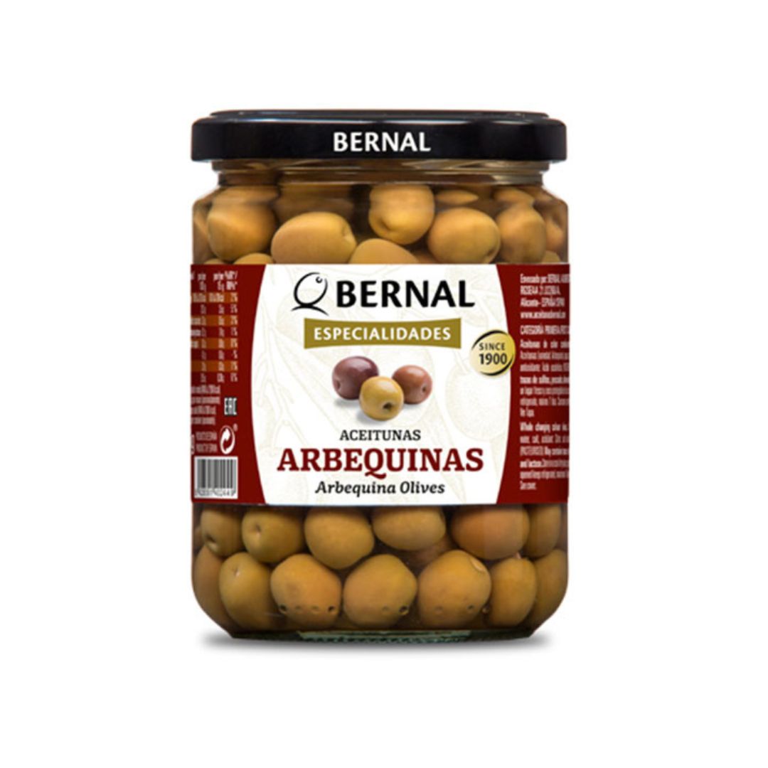 A clear jar of Bernal brand Arbequina olives, showcasing the small, round olives in brine. With a label reading "Especialidades" and "Since 1900," this classic Spanish product highlights over a century of olive-picking tradition and artisanal quality.