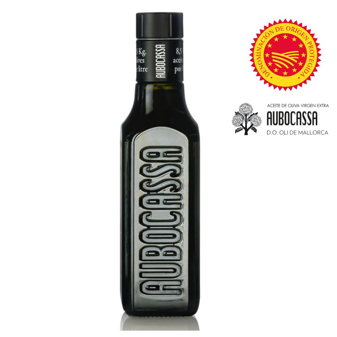 A dark glass bottle of Aubocassa olive oil with embossed branding down the front. Accompanied by D.O. Oli de Mallorca and European origin seals—authenticity and terroir in one sleek package.