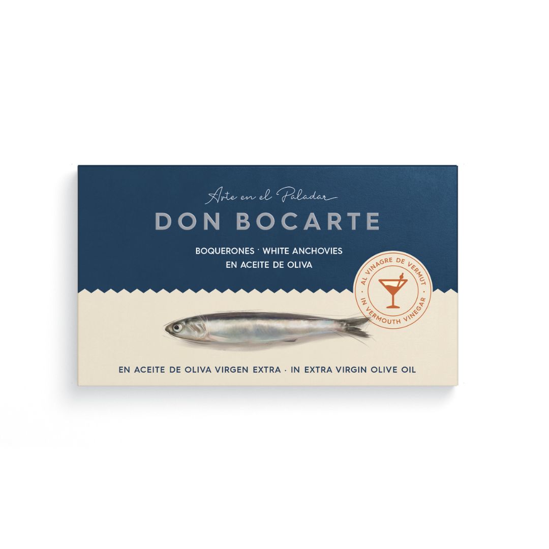 A sleek box of Don Bocarte white anchovies (boquerones) in extra virgin olive oil and vermouth vinegar. The elegant navy and cream packaging features a realistic fish illustration and a seal reading "Al Vinagre de Vermut," signaling gourmet Spanish flavor in every bite.