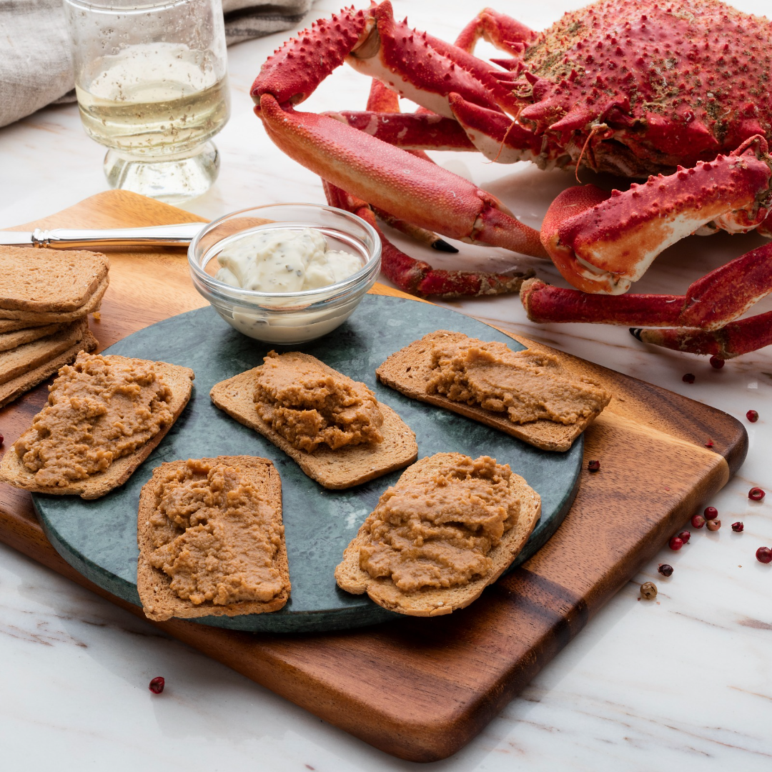5 crackers coated with crab pate. A large spider crab is in the background alongside the styled photo.