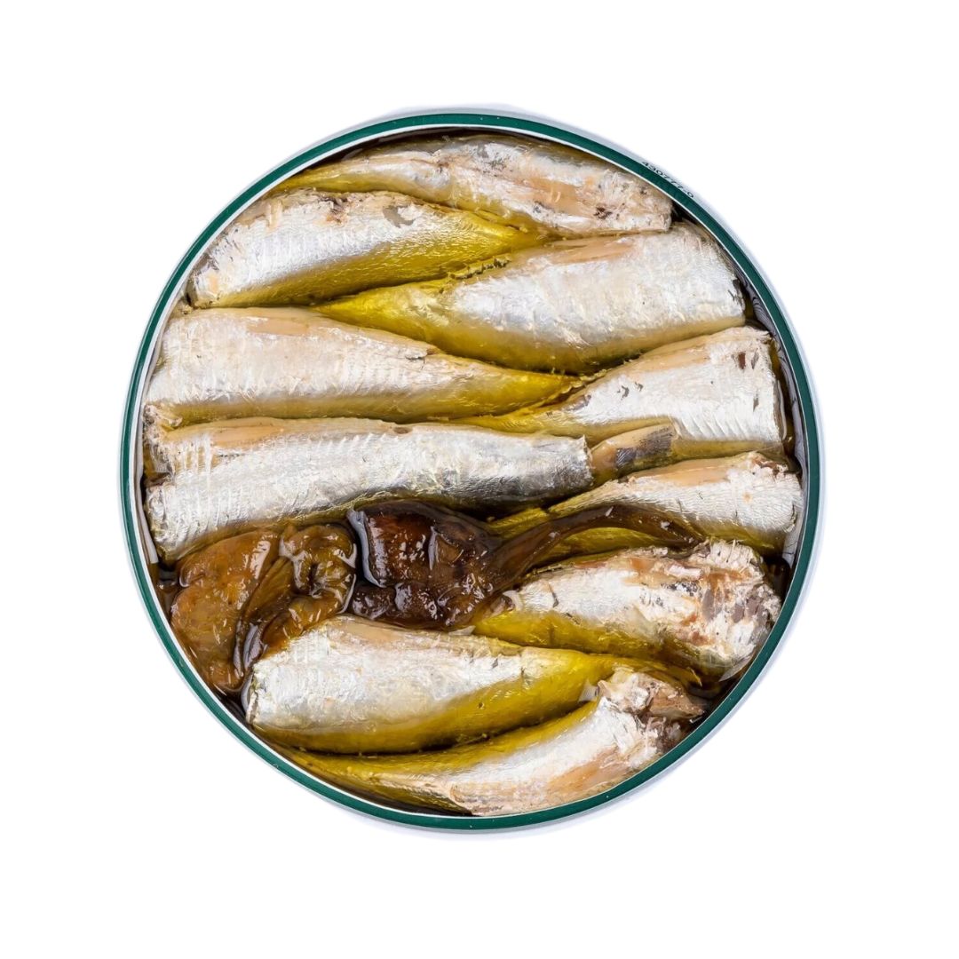 An overhead view of La Curiosa sardines tightly packed in olive oil with whole padrón peppers. The silvery fish glisten against the golden oil, while the charred green peppers add a rustic, artisanal flair.