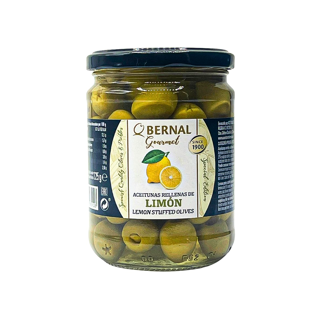 A jar of Bernal Gourmet Lemon Stuffed Olives displays plump green olives filled with bright lemon paste, packed tightly in a light brine. The label features a cheerful lemon illustration and classic gold detailing, nodding to the brand's Spanish heritage and artisanal tradition since 1900.