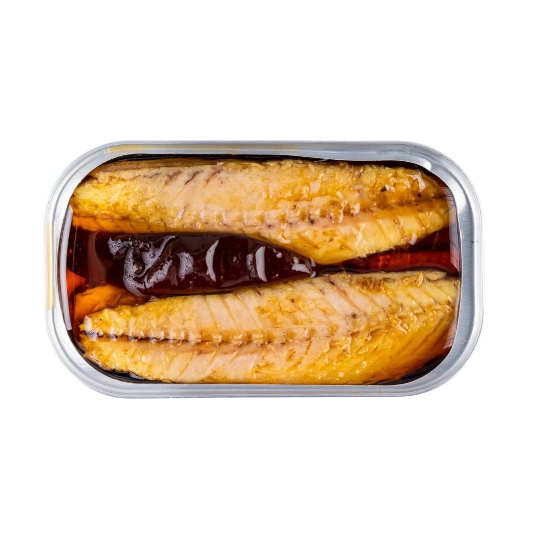 An open tin of mackerel fillets in olive oil with curry and chile. The two golden fillets are neatly arranged side by side, partially submerged in oil, with a whole dried red chile pepper placed between them. The tin is viewed from above on a white background.