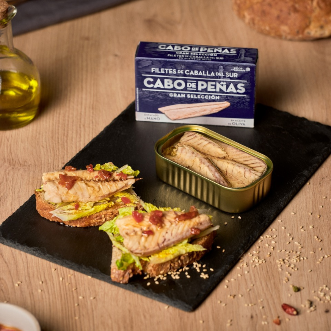 A serving board composed of two open face toasts of Cabo de Peñas mackerel and other garnishes.