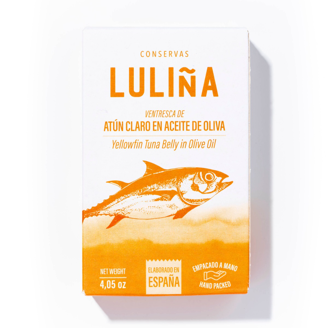 A bold, sun-drenched box of Luliña yellowfin tuna belly catches the eye with its striking orange fish illustration and warm ombré fade. Printed with clean, modern typography in both Spanish and English, it highlights the tuna's premium cut—ventresca—preserved in olive oil and proudly hand-packed in Spain.