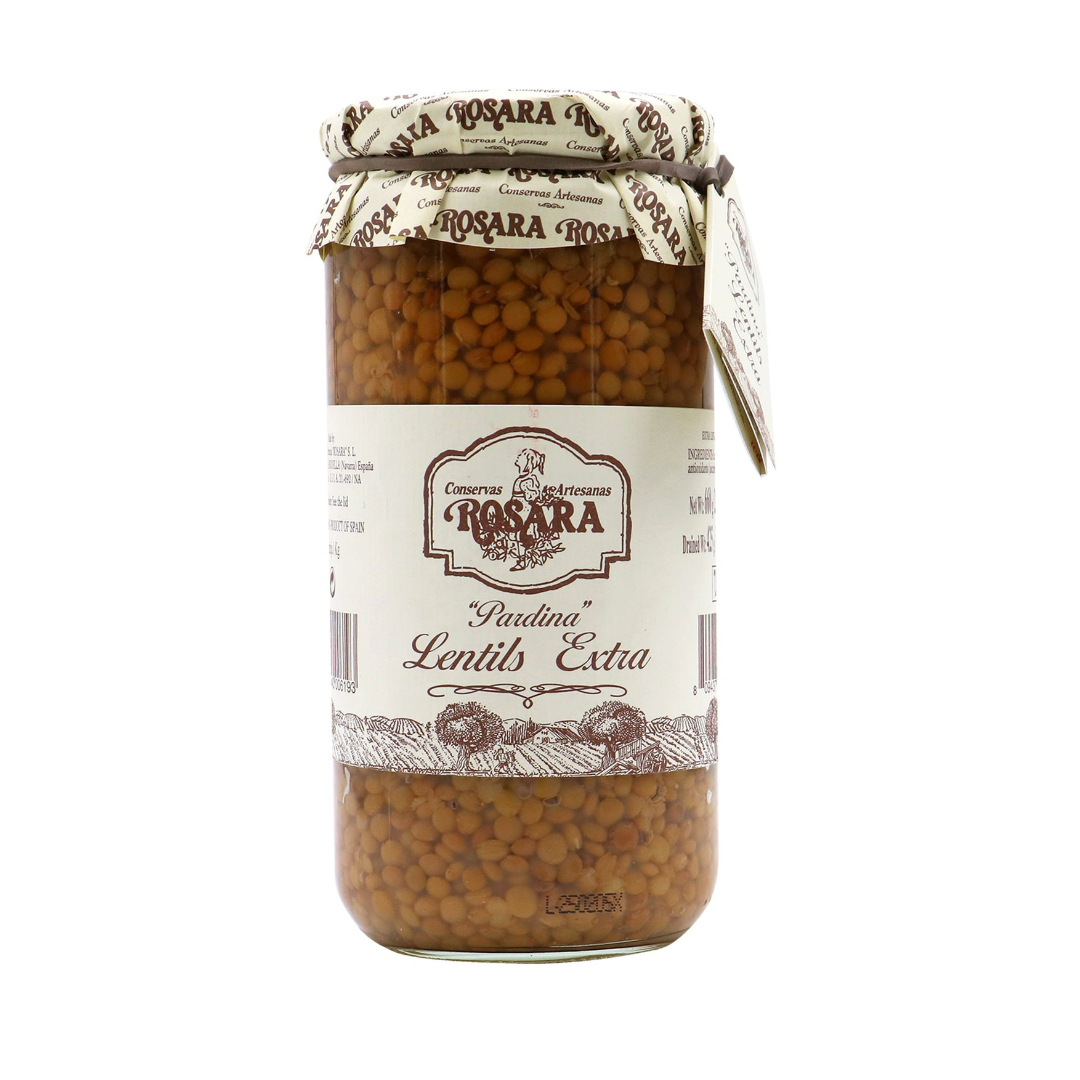 A tall jar of Rosara "Pardina" Lentils Extra stands proudly, its rustic cream-and-brown label featuring hand-drawn fields and the Rosara crest. Through the clear glass, the small, tender lentils are tightly packed, their earthy hue hinting at the rich flavor inside. A paper-wrapped lid and attached tag complete the artisanal, traditional look.