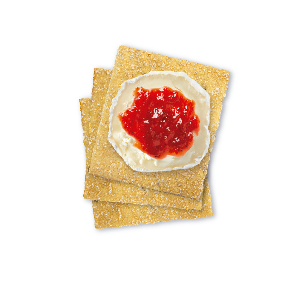 Three square sweet olive oil crackers stacked on top of each other, with the top cracker topped with a spread of creamy white cheese and a dollop of bright red jam.