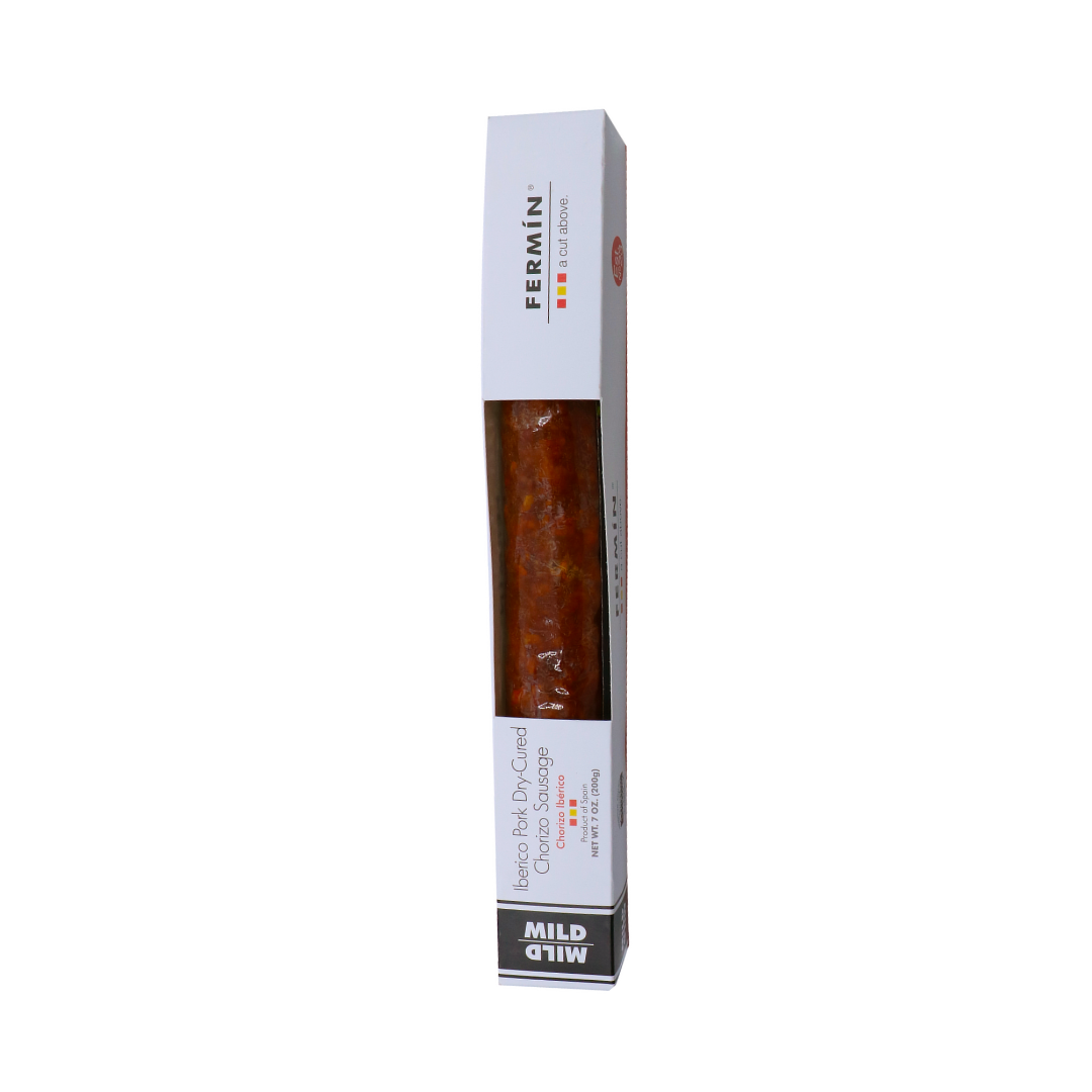 A vacuum-sealed package of Fermin Iberico dry-cured chorizo sausage. The packaging is sleek and white with the Fermin logo at the top. The sausage is a rich reddish-brown color and is labeled as "MILD" at the bottom. The packaging also specifies that the product is made from Iberico pigs and is dry-cured, showcasing a premium Spanish product.