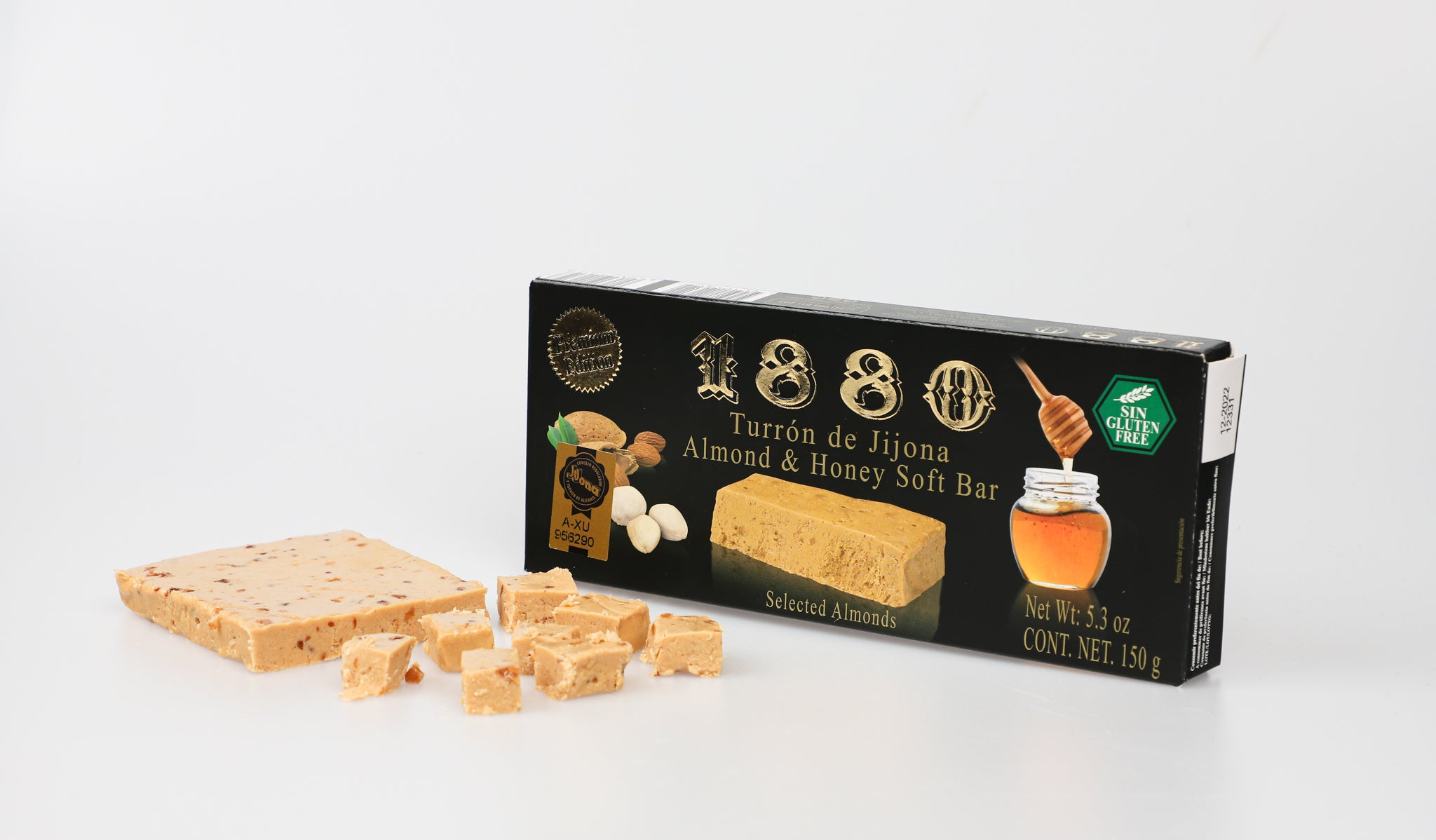 A slab of soft turrón sits partially sliced beside its elegant black 1880 box. The nougat’s smooth, golden texture is dotted with bits of almond, while small cubes are neatly cut in front, showcasing its tender, melt-in-the-mouth consistency. A classic Spanish treat, now ready to serve.