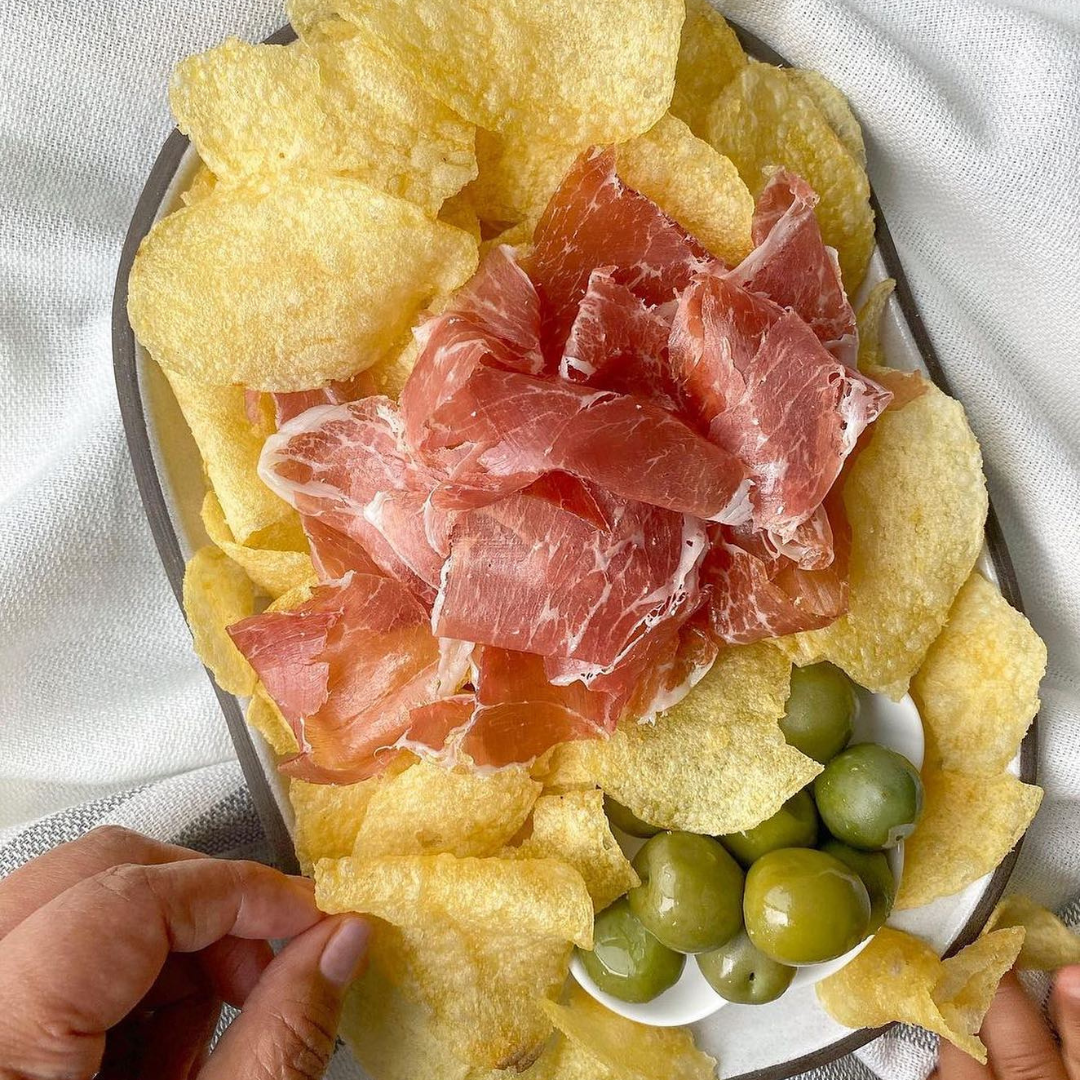 Bonilla a la vista chips served on a platter, alongside jamón ibérico and olives.