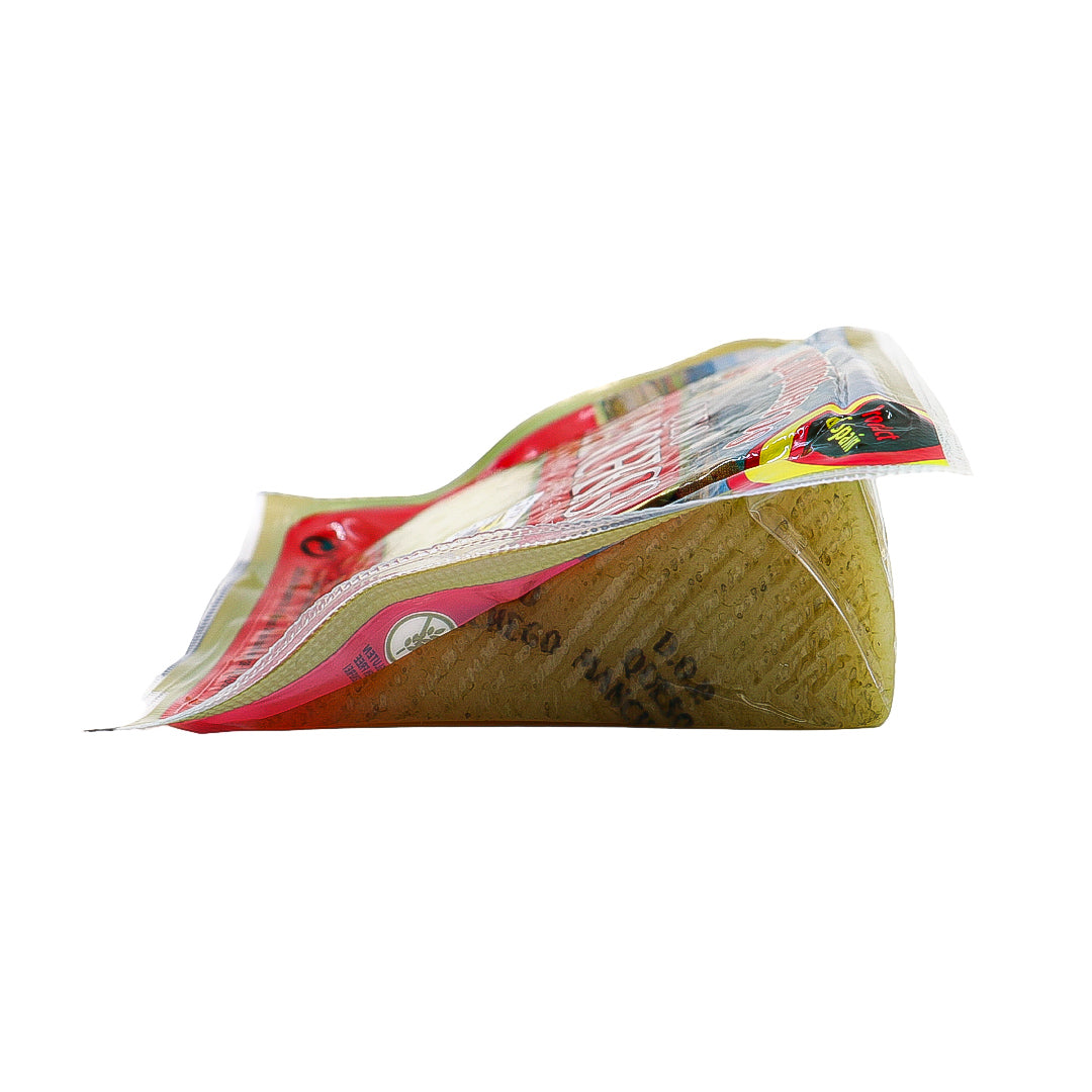 A side view of Los Carpinteros Manchego cheese reveals its signature zigzag rind pattern through the vacuum-sealed packaging. This firm wedge of DOP-certified cheese hints at its artisanal aging and bold Spanish character.