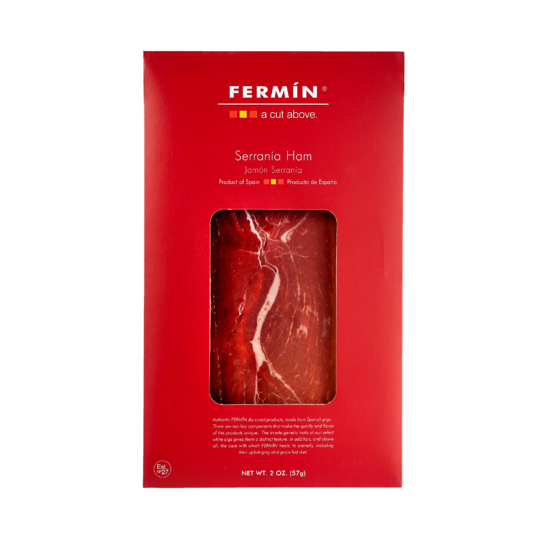 A vibrant red box of Fermín Serranía Ham highlights premium Spanish charcuterie. The window reveals thinly sliced jamón serrano with rich marbling. Elegant branding and a clean design emphasize its artisanal quality—perfect for tapas, gourmet boards, or elevated snacking.