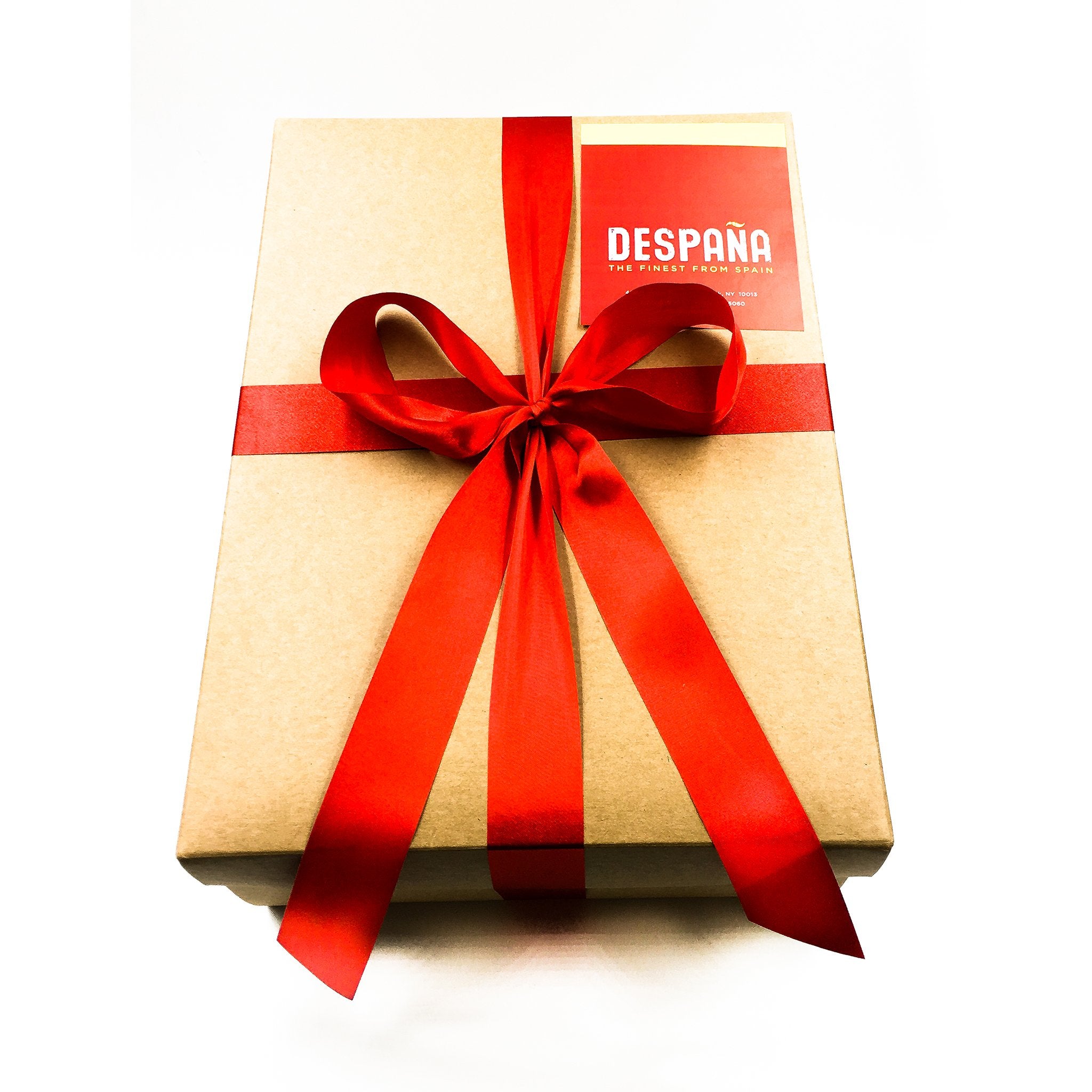 A kraft gift box wrapped in a bold red ribbon and finished with a bow. The “DESPAÑA” label on the top right marks it as a premium Spanish food gift—simple, elegant, and ready to impress.