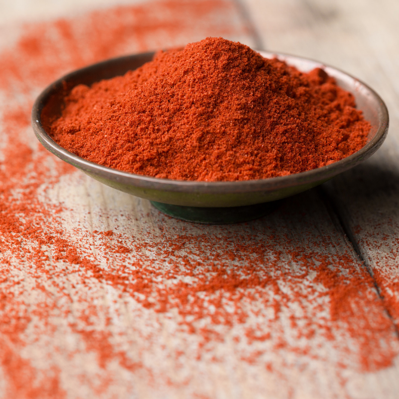 A small spice bowl of paprika sitting on a table dusted with paprika. 