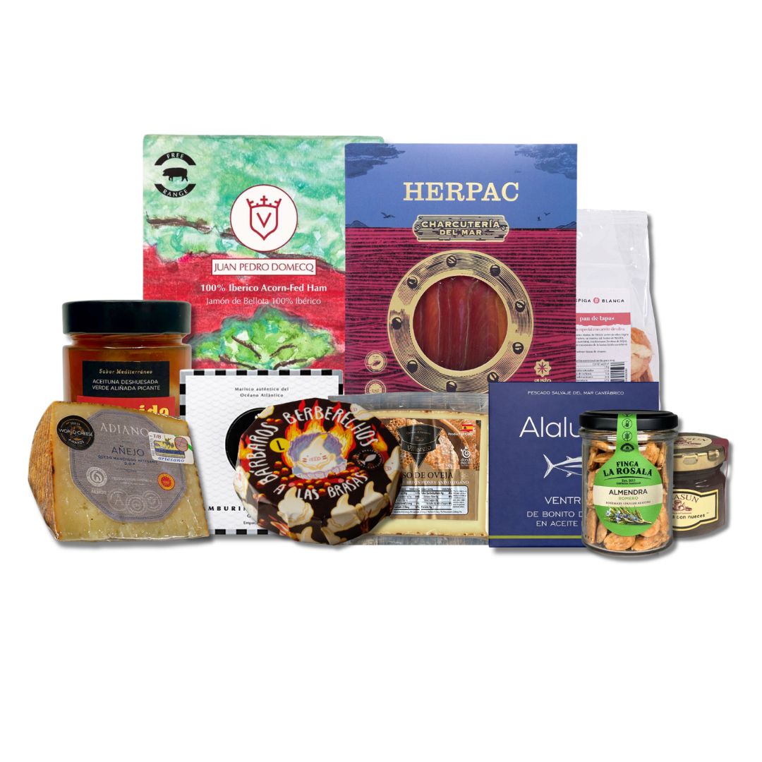 A gourmet food gift hamper featuring a variety of packaged products including a block of cheese, a jar of honey, a round cheese wheel, a box of crackers, and several packaged snacks and spreads, arranged together on a white background.